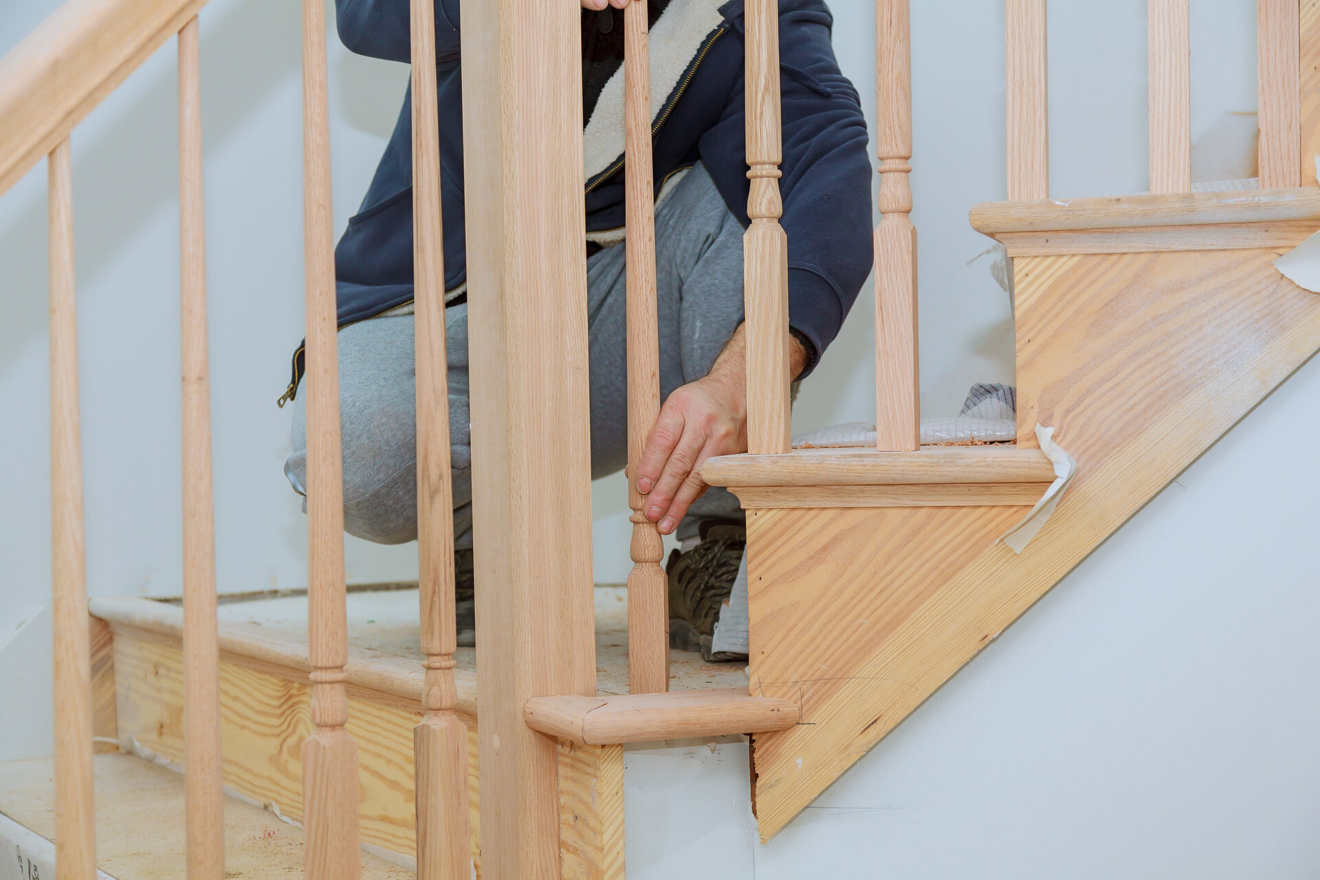 Mann installiert ein Holz-Treppengeländer an einer Treppe.