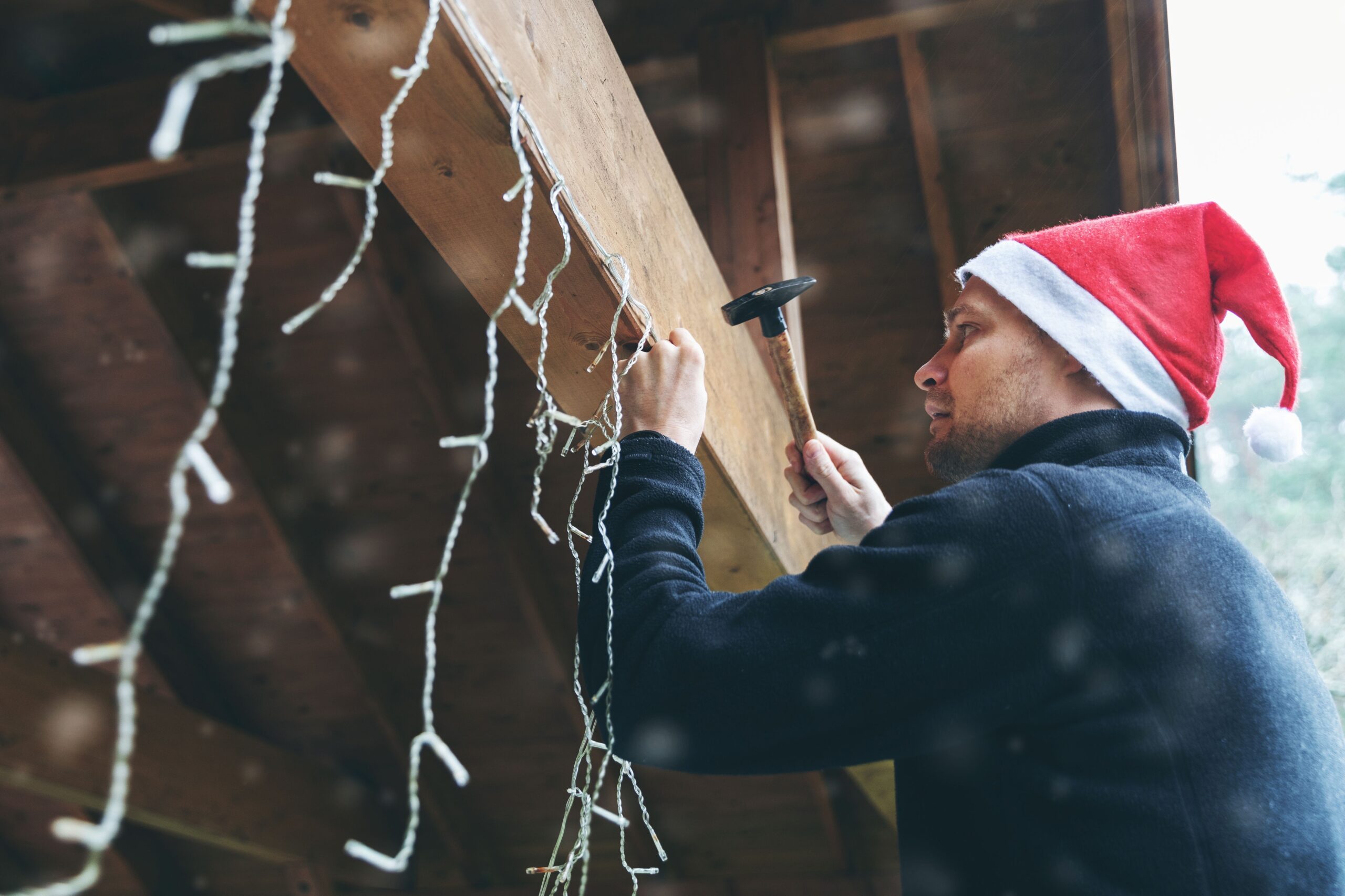 Mann mit Weihnachtsmütze dekoriert das Haus im Freien am Carport mit Weihnachtslichterketten.